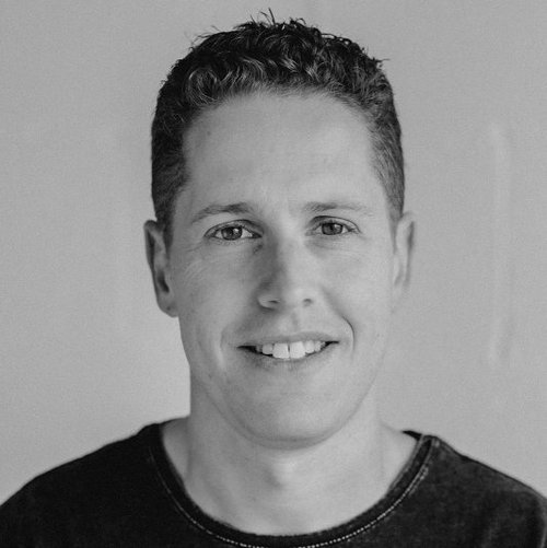 Black and white portrait of Daniel Taft, smiling, in a dark t-shirt.