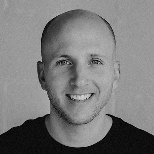 Black and white portrait of Udi Zuriel, smiling, in a dark t-shirt.